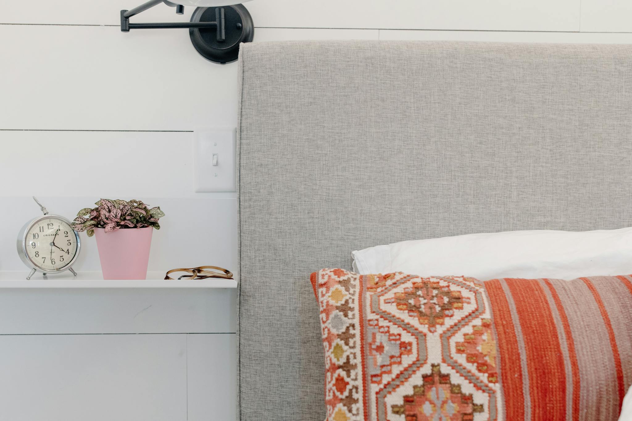 Modern bedroom decor featuring a bohemian cushion, potted plant, and vintage clock.